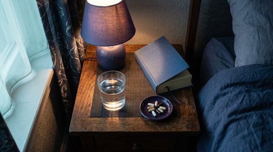 Comodino con integratori per dormire, bicchiere d'acqua e luce soffusa serale